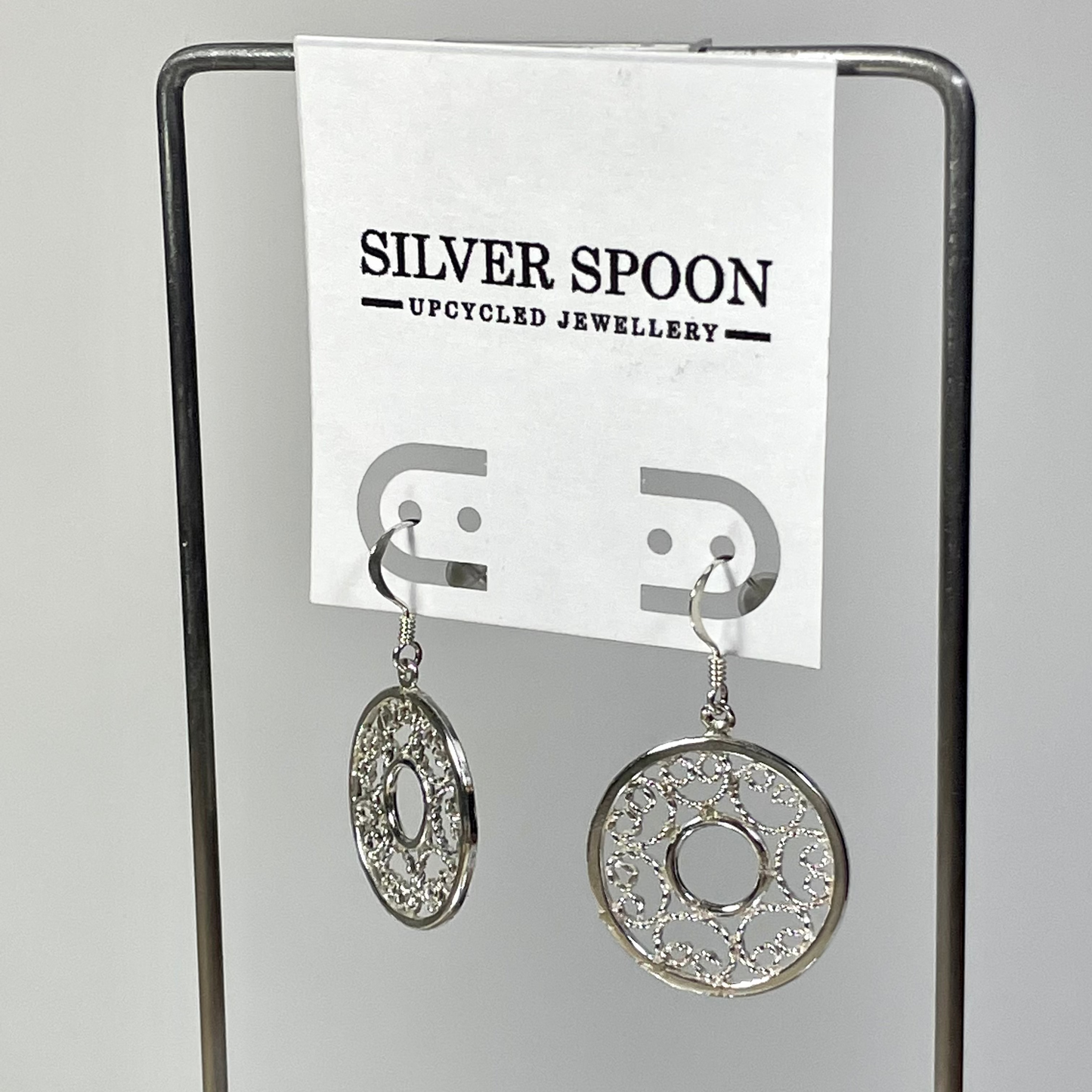Silver spoon earrings on a stand with 'Silver Spoon Upcycled Jewellery' label.