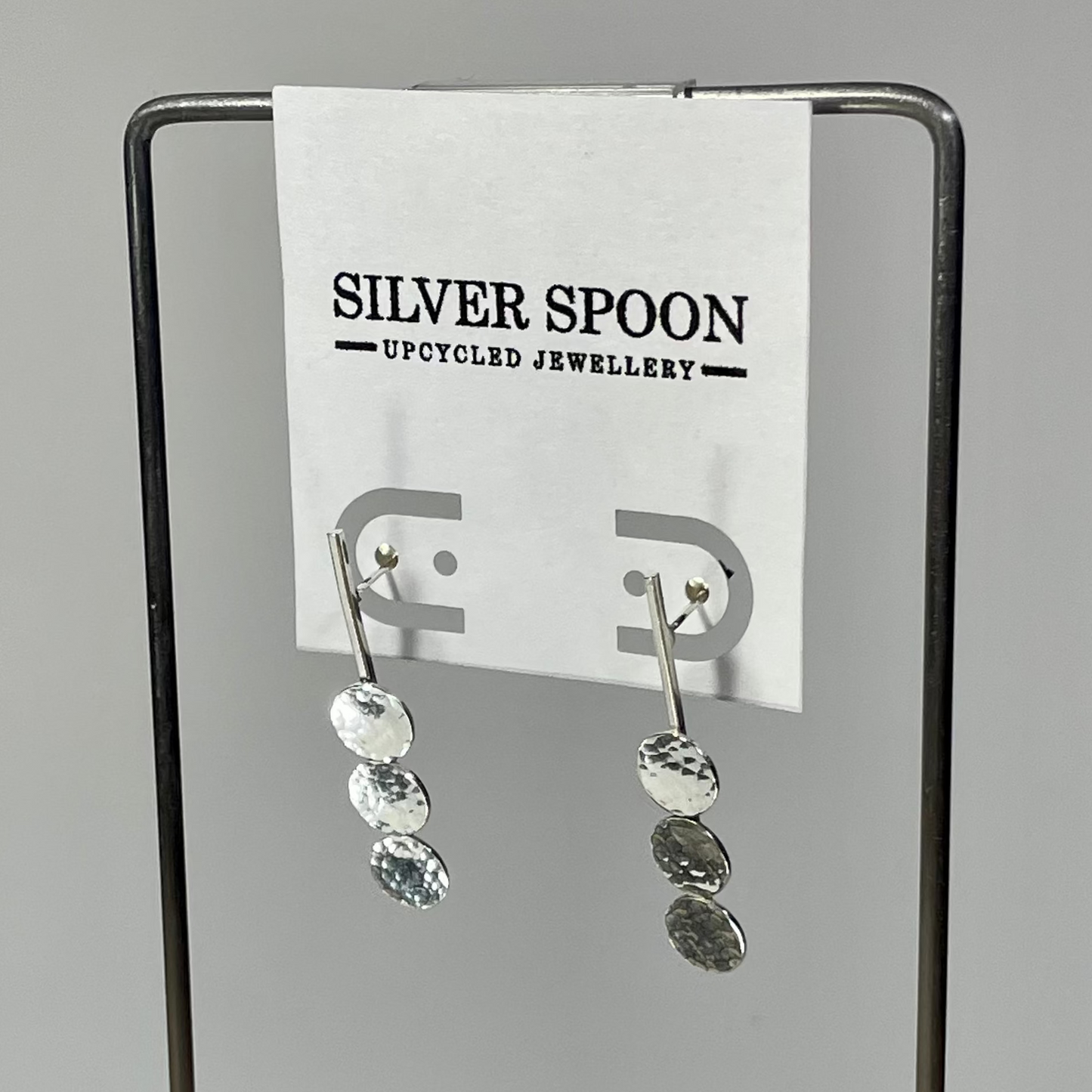 A pair of sterling silver post earrings displayed on a card stand, with the brand name 'Silver Spoon' visible in the background.