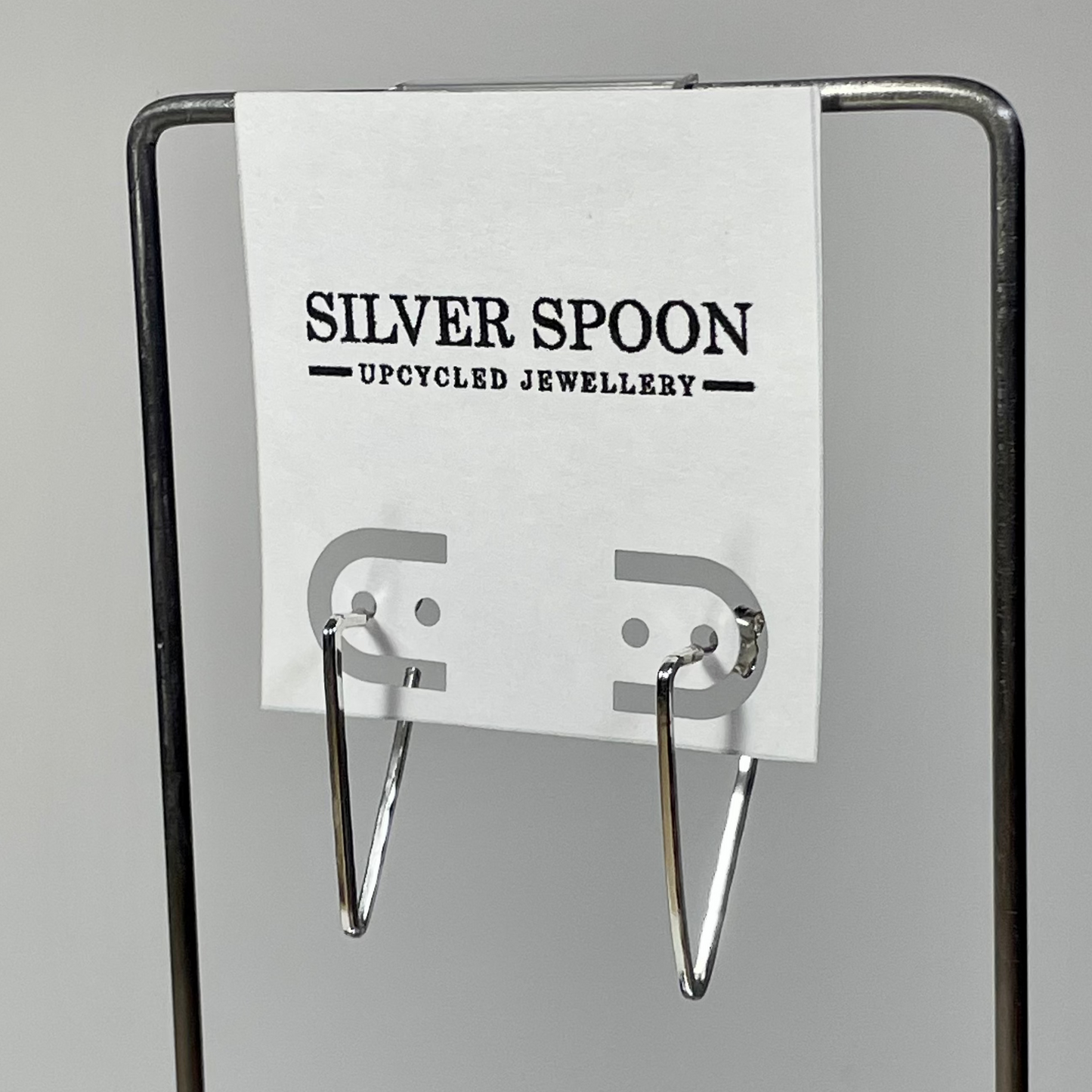 A pair of triangular silver post earrings displayed on a card that reads 'Silver Spoon Jewellery, Recycled Jewellery'.