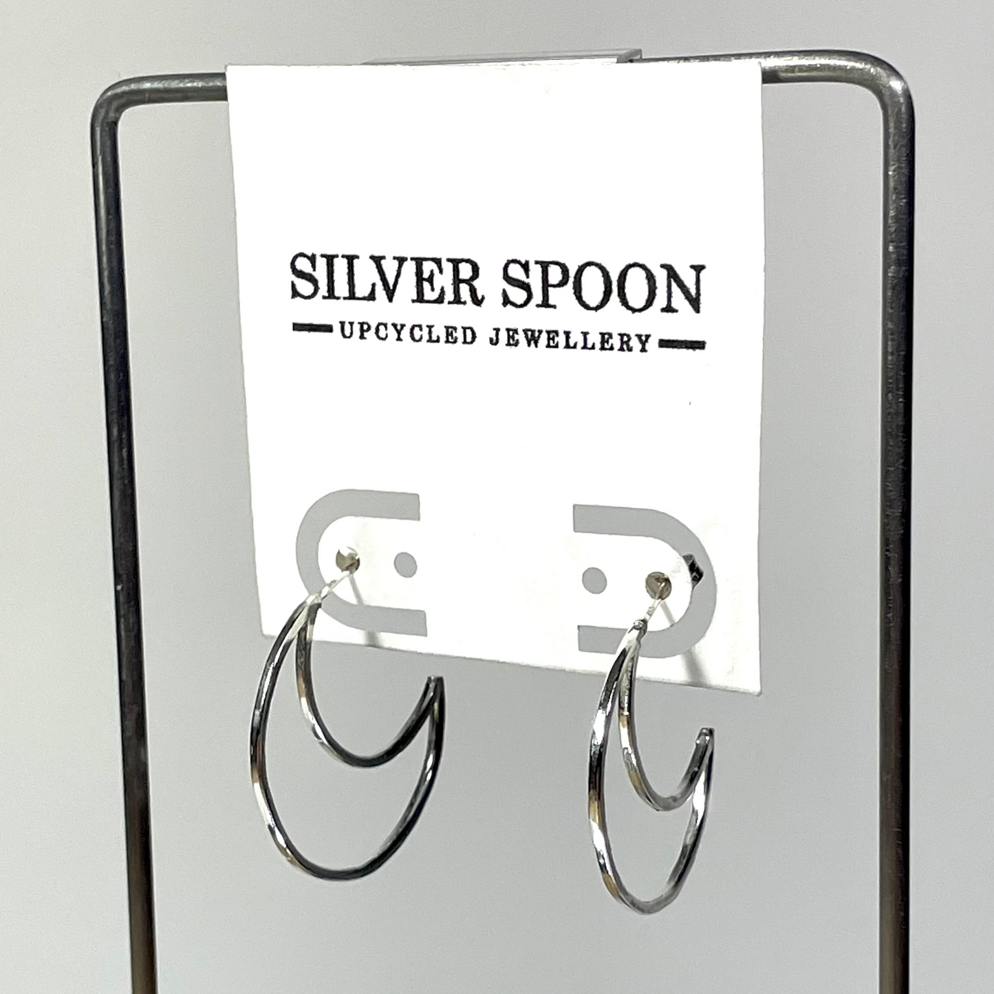 Silver spoon earrings on a stand with 'Silver Spoon Upcycled Jewellery' label.