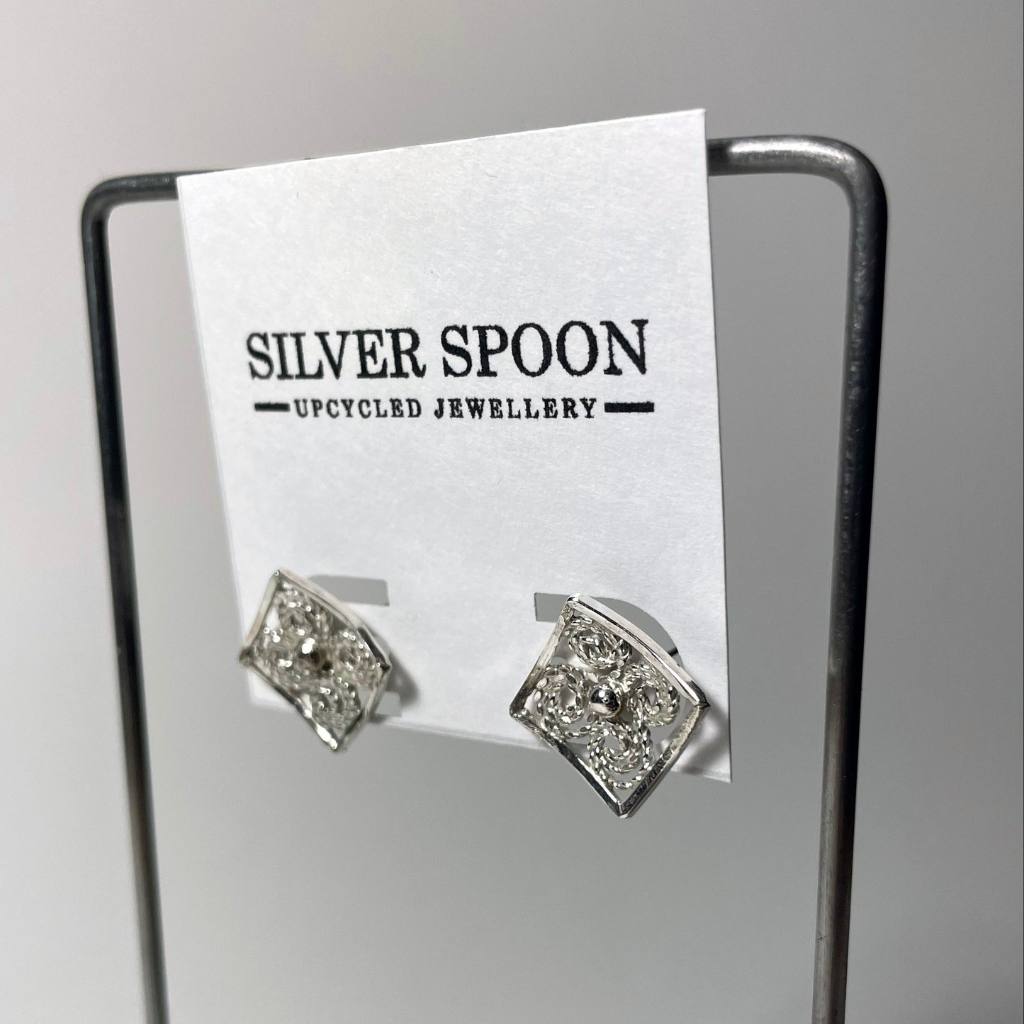 A pair of sterling silver filigree post earrings displayed on a stand, with the brand name 'Silver Spoon' visible at the top.