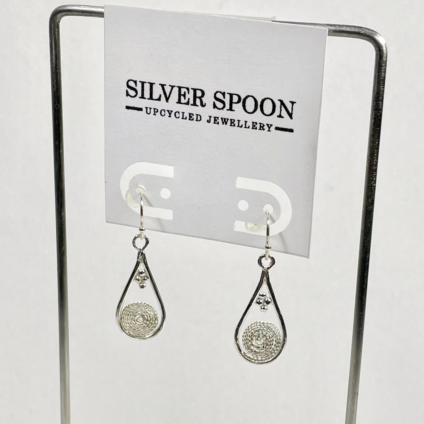 A pair of sterling silver filigree earrings displayed on a stand with the brand name 'Silver Spoon' visible in the background.
