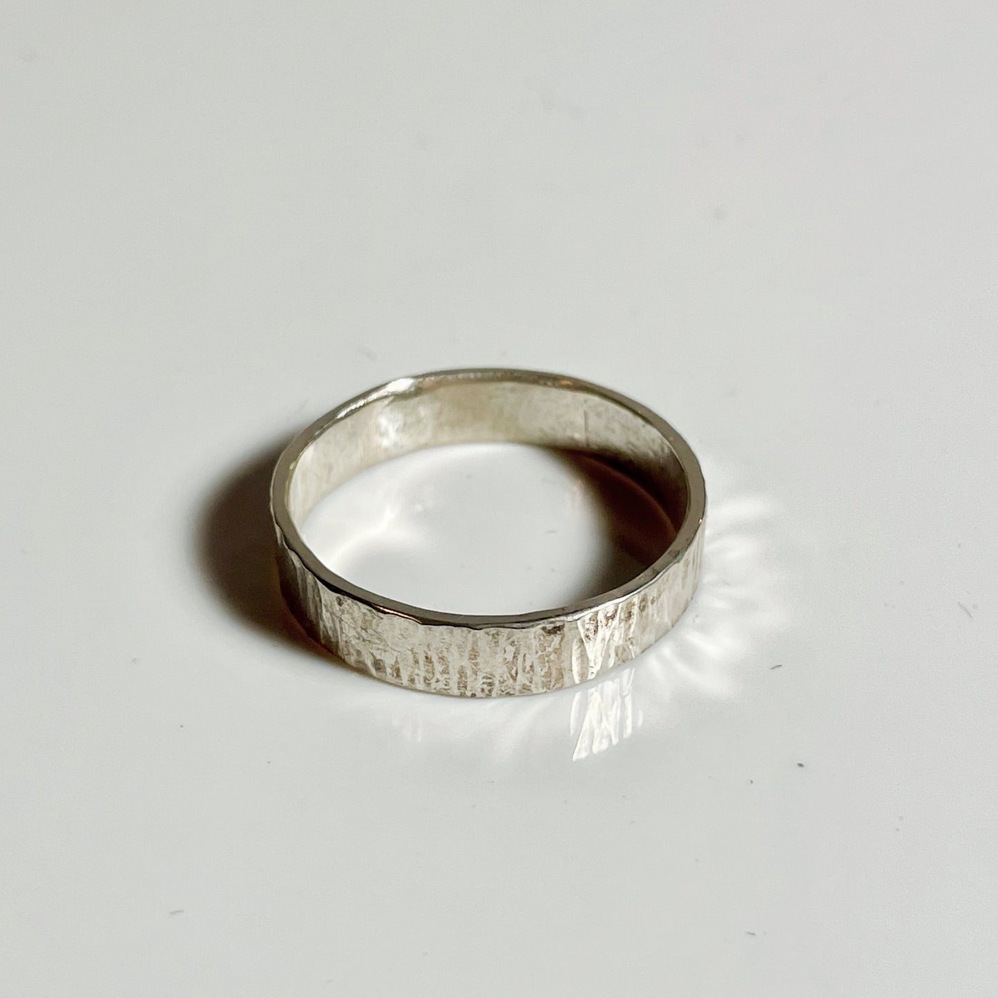 A 3mm sterling silver band ring with horizontal hammered texture on a white background.