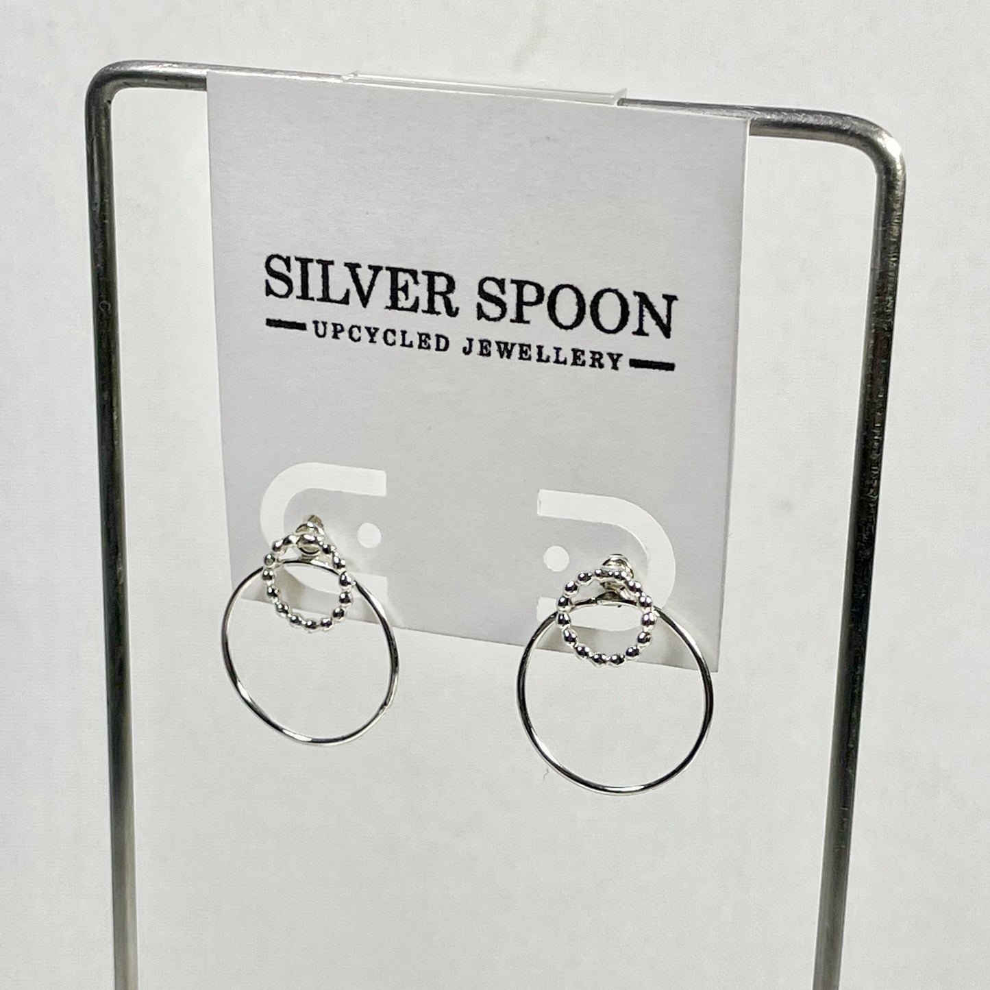 A pair of sterling silver post earrings displayed on a stand with the brand name 'Silver Spoon' visible in the background.