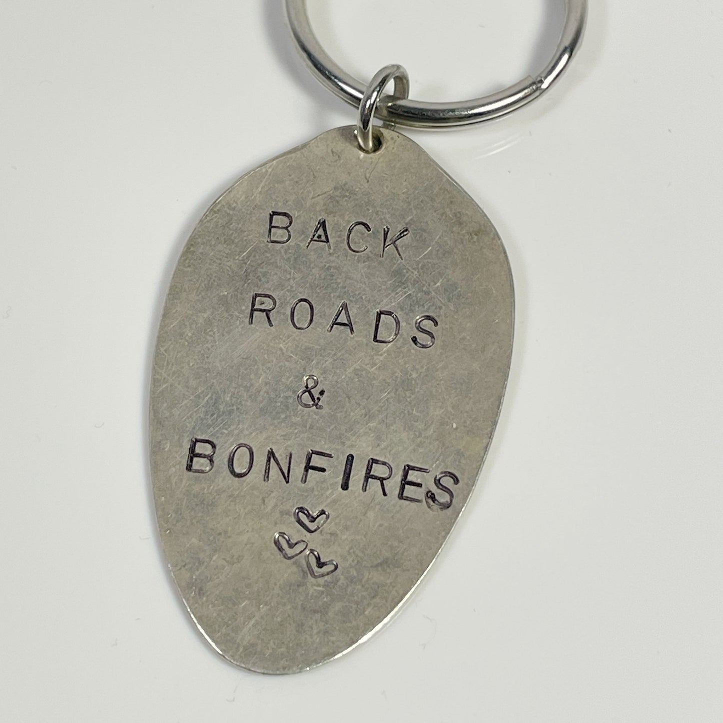 A silver-colored keychain with 'BACK ROADS & BONFIRES' and 'SPOON' stamped on it.