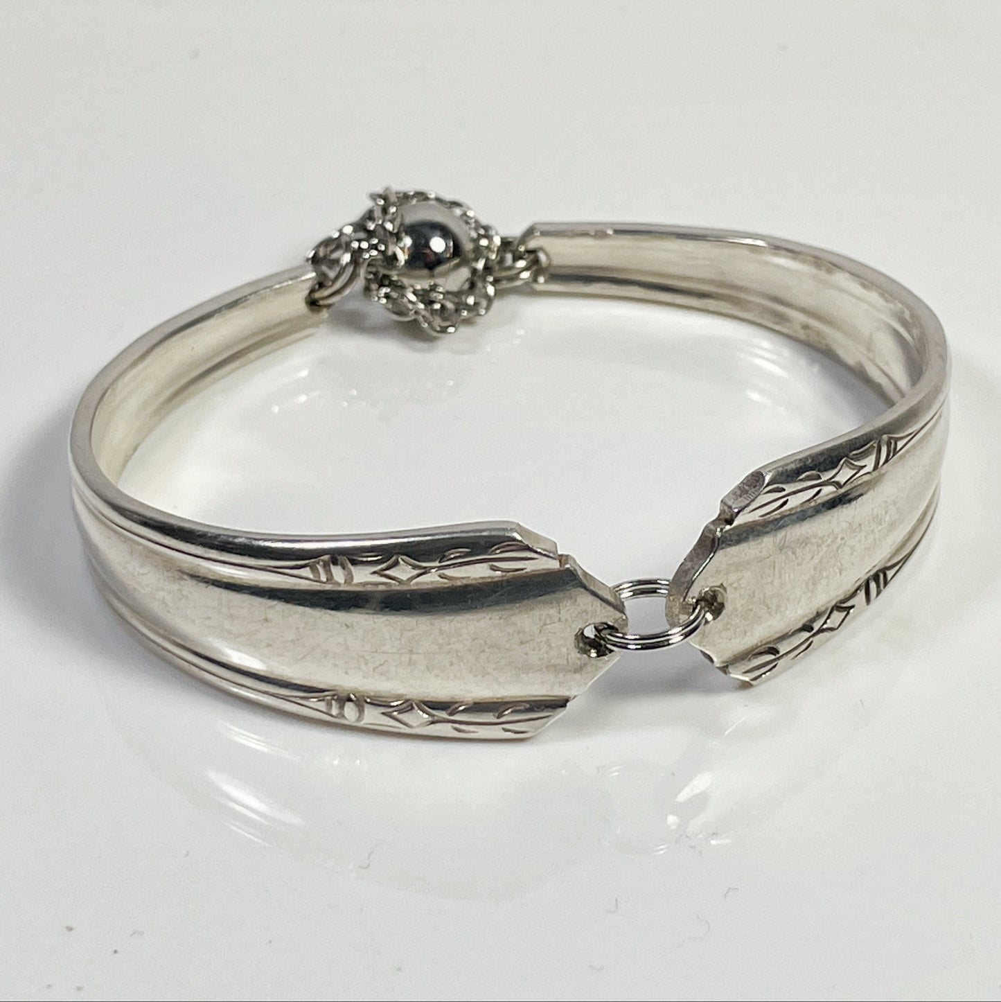 A silver spoon handle bracelet with a split jump ring and safety chains.