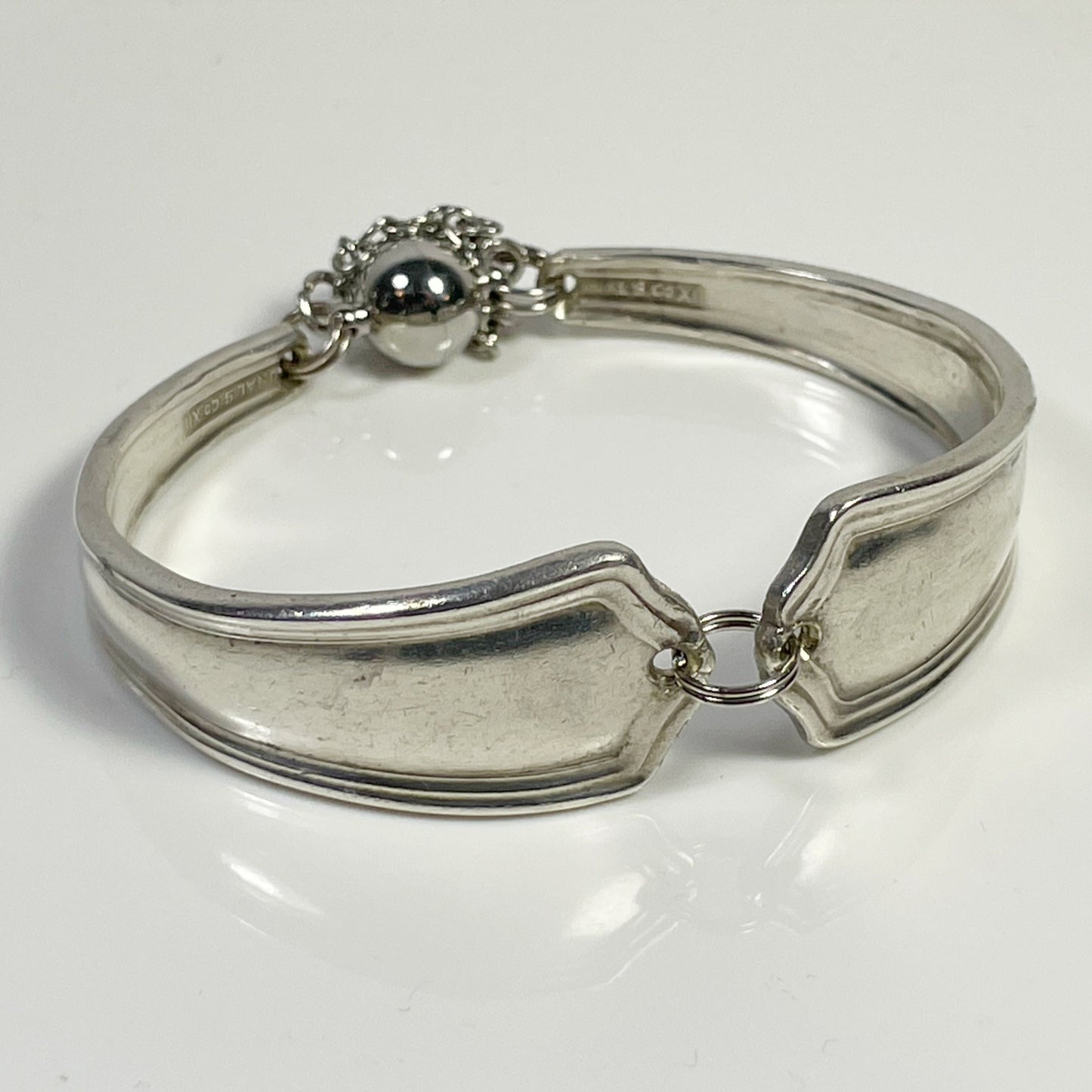 A silver spoon handle bracelet with a split jump ring and safety chains.