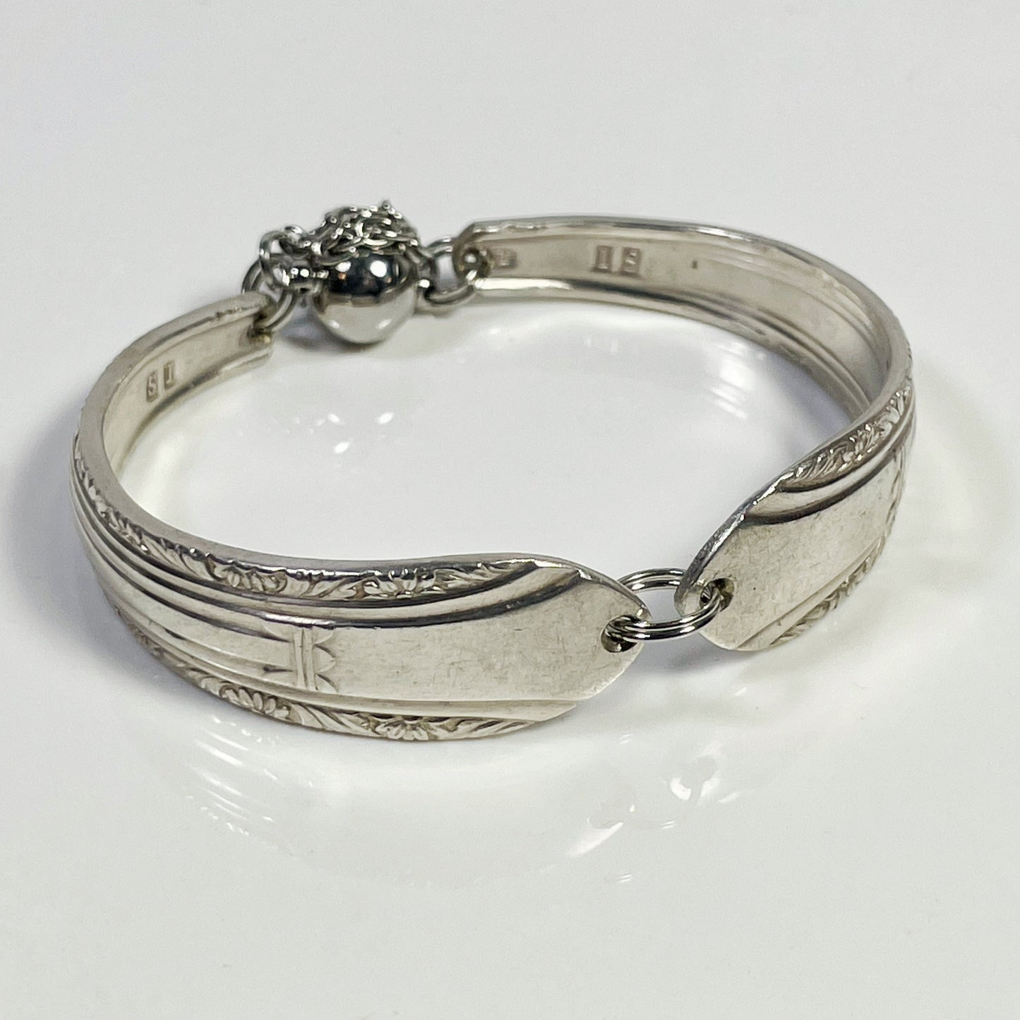 A silver spoon handle bracelet with a split jump ring and safety chain.
