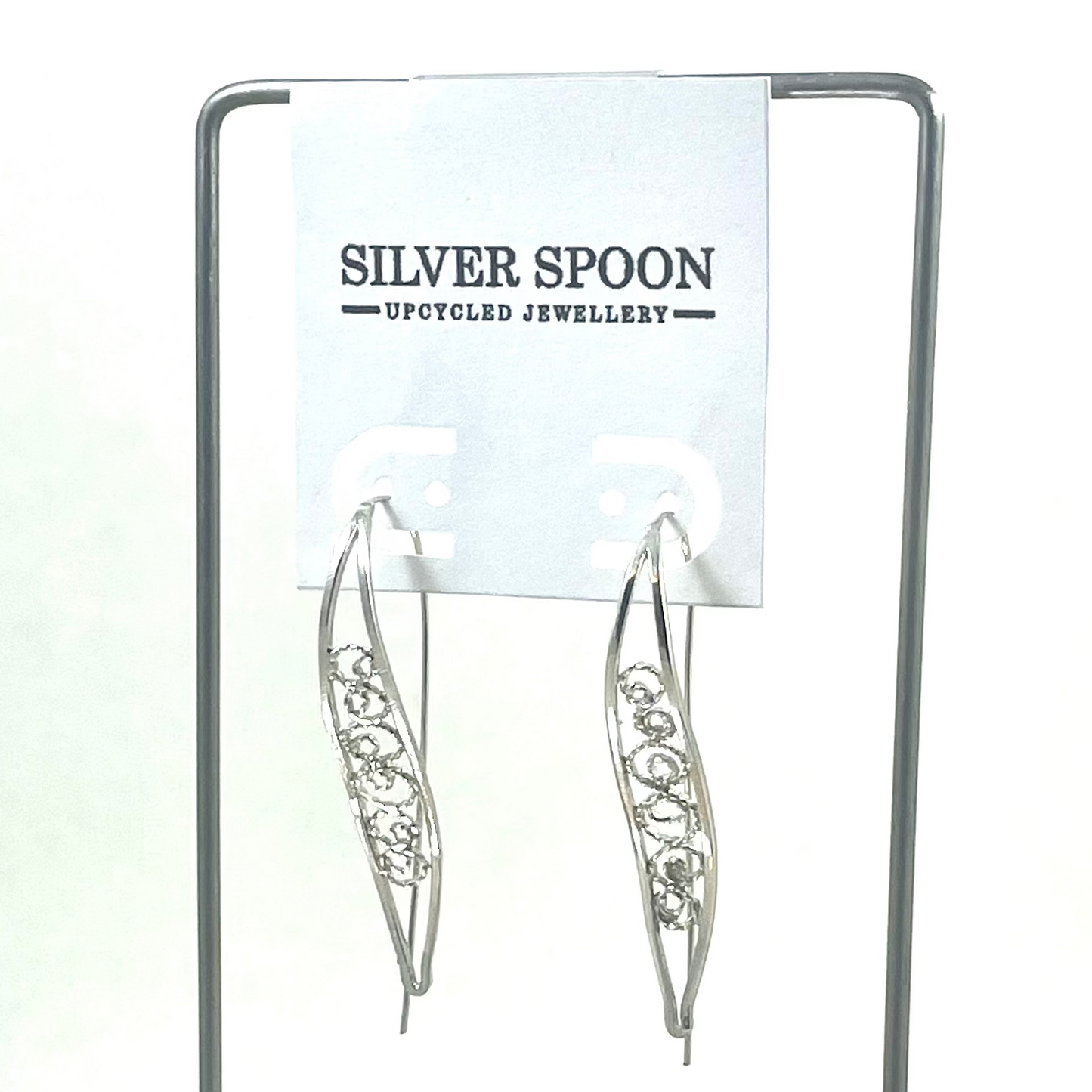 A pair of sterling silver filigree hook earrings displayed on a wooden stand with a branded card above.