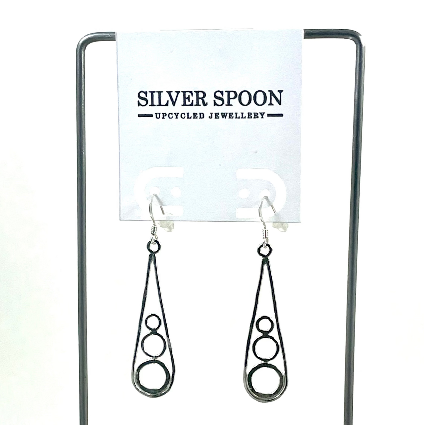 A pair of sterling silver drop earrings displayed on a stand with the brand name 'Silver Spoon' visible in the background.