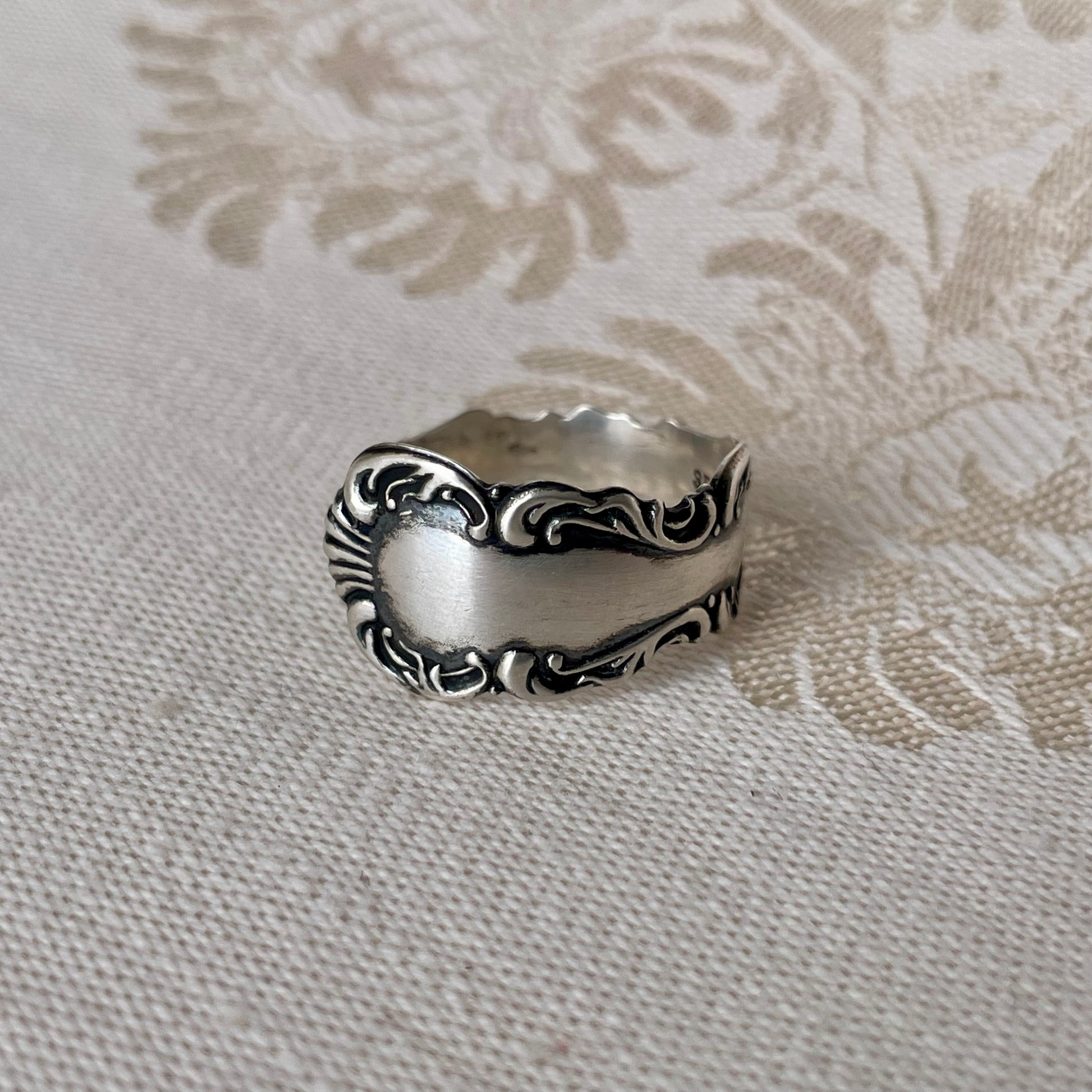 Silver ring with intricate design on a textured beige background