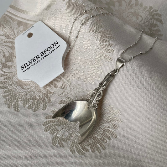 Silver spoon with a decorative handle on a textured fabric background, featuring a 'Silver Spoon' tag.