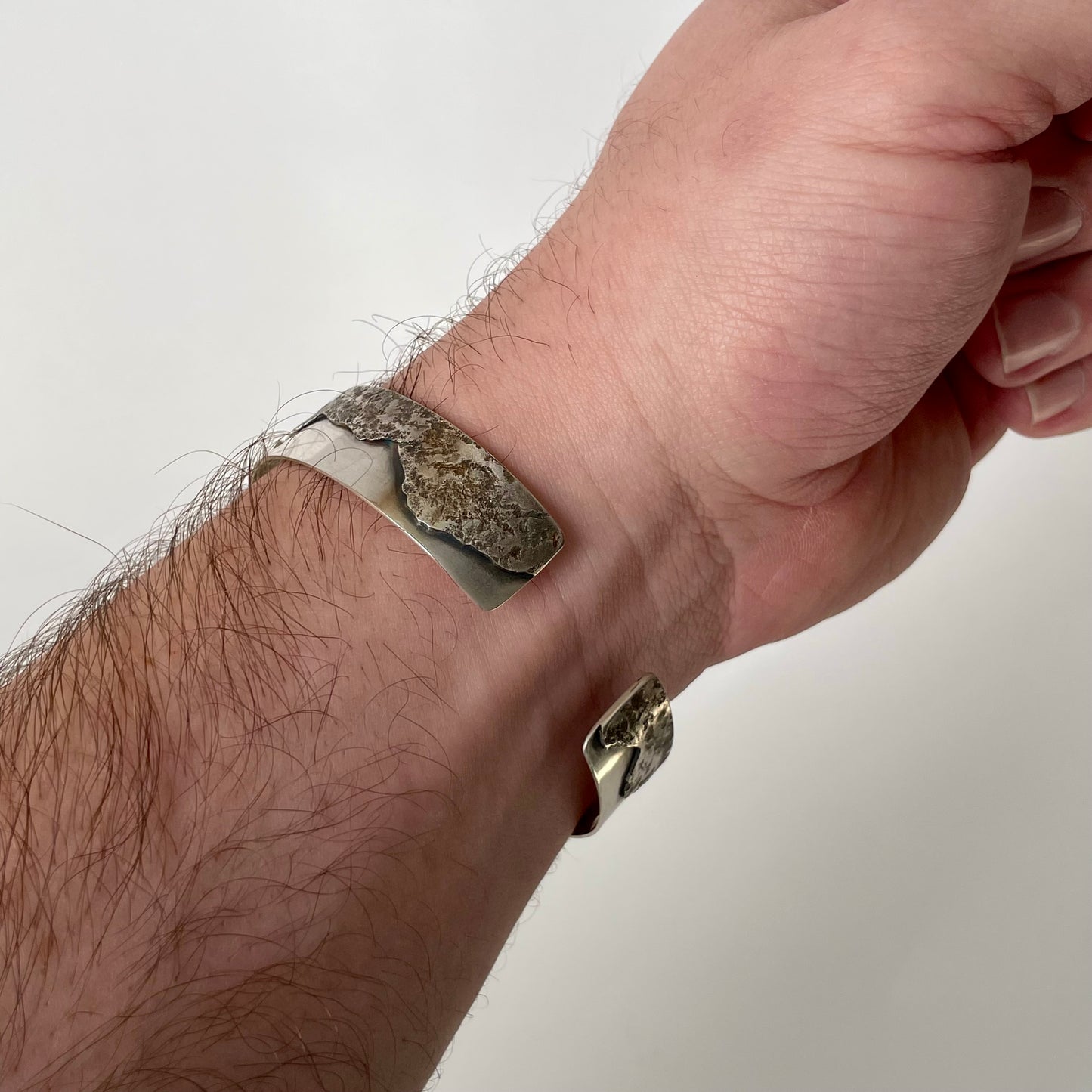 Hand wearing a textured silver bracelet on a plain background