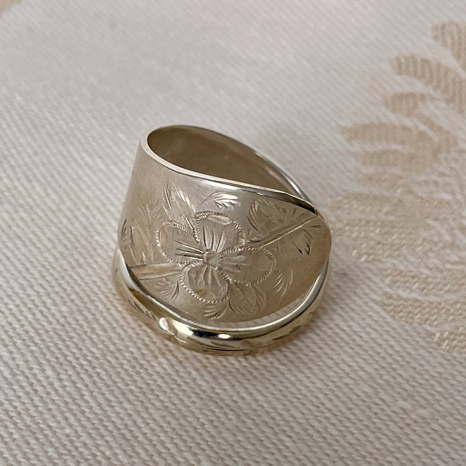 Silver ring with engraved design on a textured fabric background