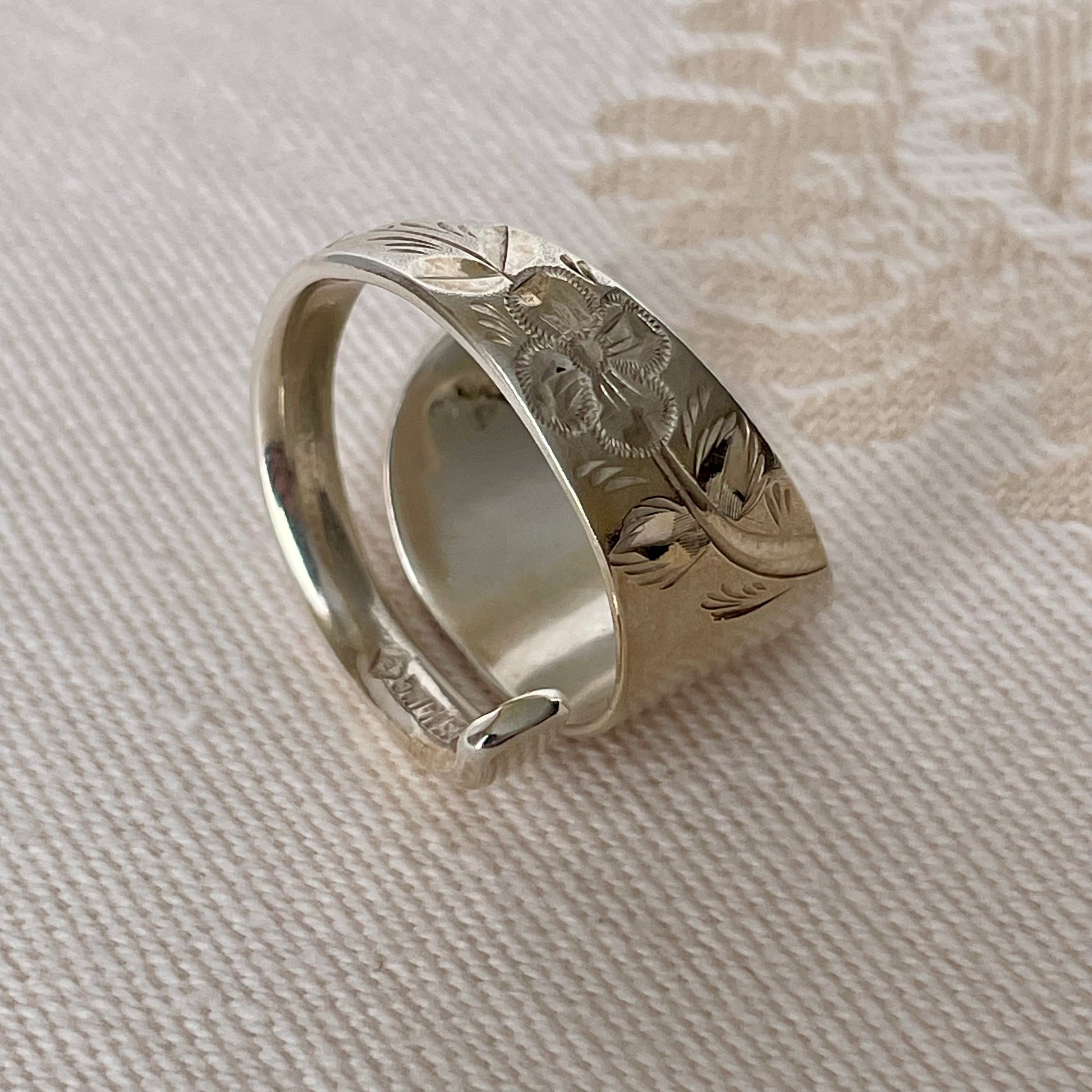 Silver ring with floral engraving on a textured beige fabric background