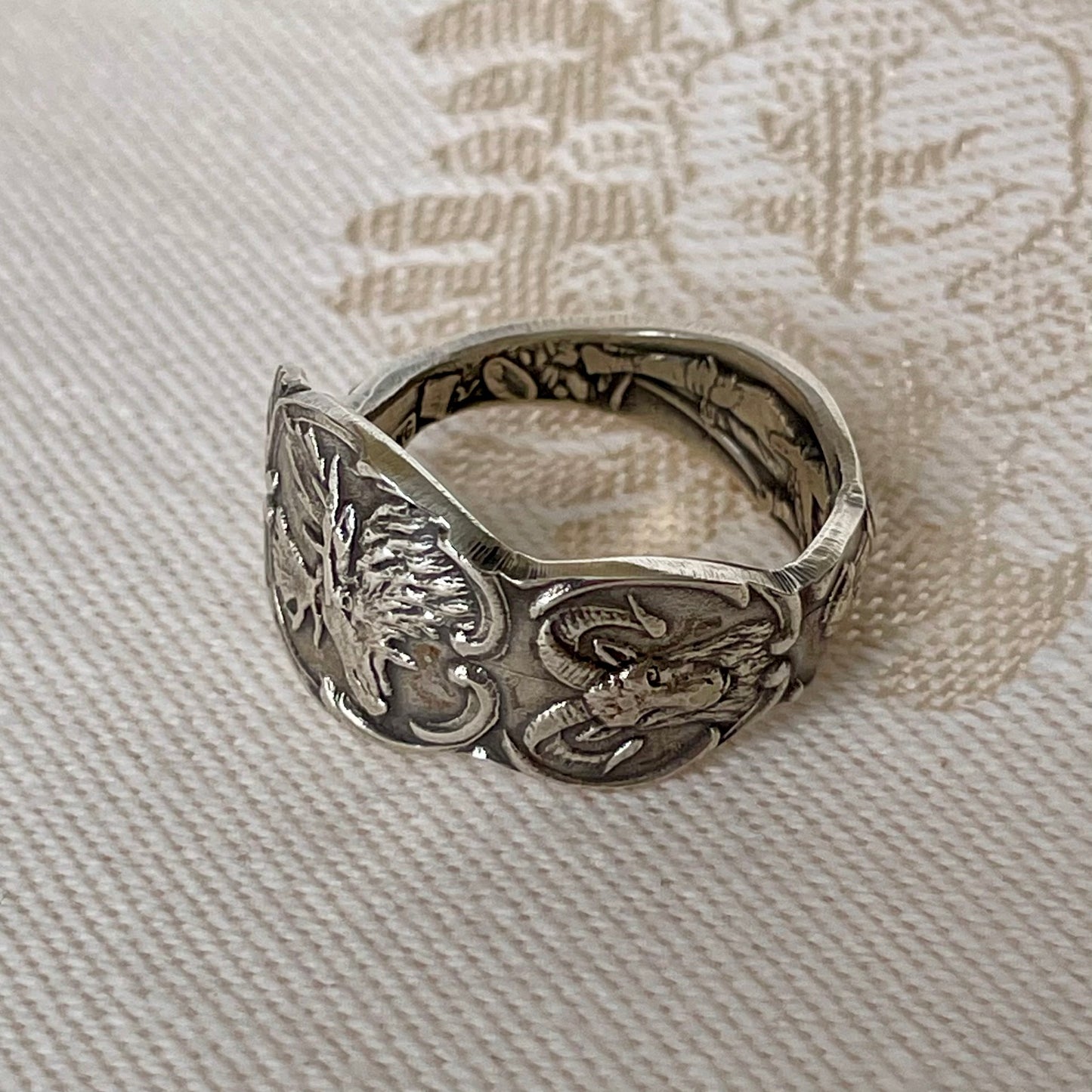 Silver ring with detailed design on a textured fabric background