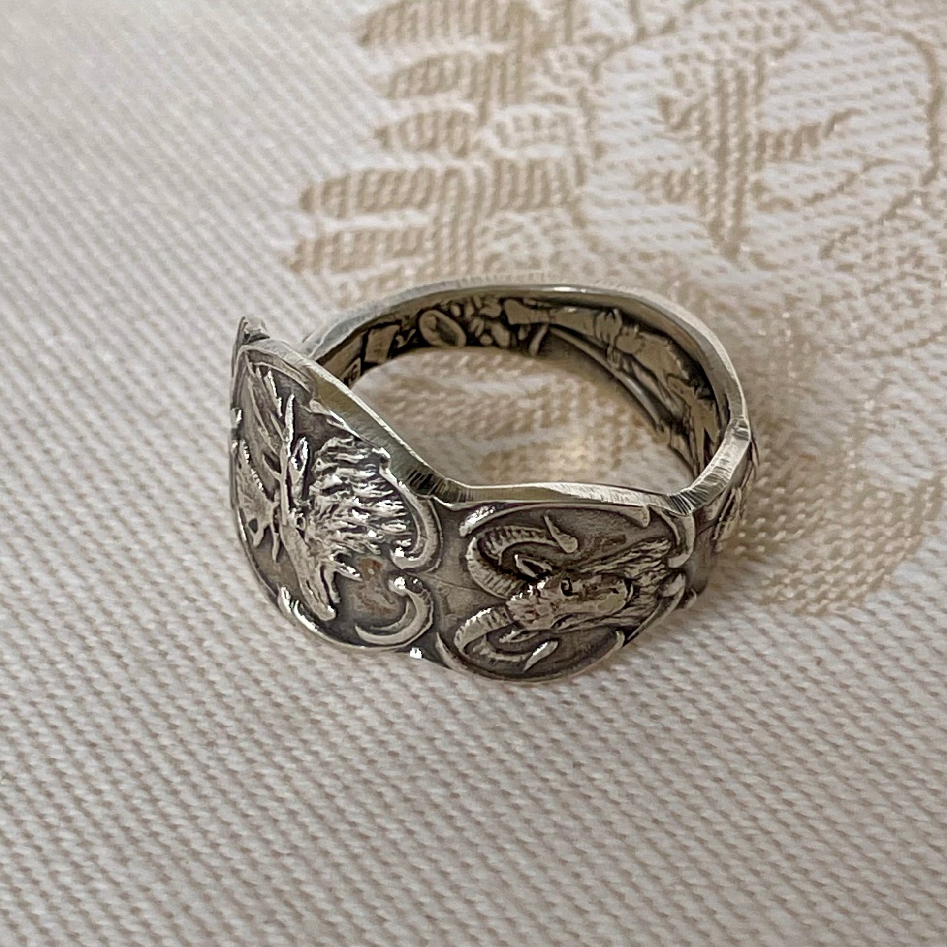 Silver ring with detailed design on a textured fabric background